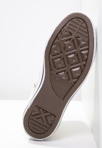 Semelle en caoutchouc tan avec un motif en diamant texturé et un liseré blanc ; présente un logo embossé sur la semelle intermédiaire pour identification.