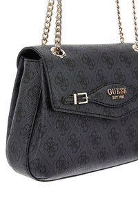 Borsa nera texturizzata con tracolla in catena dorata. Presenta un clasp e un motivo in rilievo, con il marchio "GUESS EST 1981" in lettere dorate.