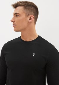 Svart långärmad T-shirt i bomull med rund halsringning. Har en liten vit broderad hummerlogotyp på bröstet.