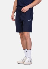Shorts en coton bleu marine avec taille élastique et cordon de serrage. Présente un logo brodé sur le côté. Coupe décontractée, longueur mi-cuisse.