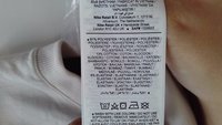 Oznaka za oblačilo, večinoma v beli barvi, z navodili za nego in podatki o materialu: 81% poliester, 13% bombaž, 6% elastan.