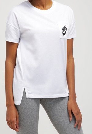 Osoba ubrana w białą koszulkę Nike z logo na przedniej kieszeni, połączoną z szarymi legginsami, pokazana od szyi do połowy uda.