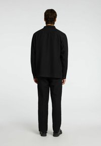 Sort button-up skjorte og matchende bukser, begge i et tekstureret stof. Enkelt design med lange ærmer og lige ben.