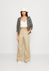 Lightweight, dark green jacket over a white cropped top, paired with high-waisted beige wide-leg pants and white sneakers. White bucket hat.
