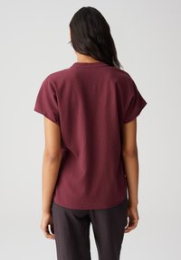 Top corto in tonalità bordeaux, con texture, scollatura rotonda e vestibilità rilassata, abbinato a pantaloni scuri e larghi.