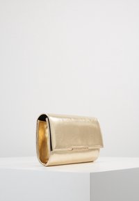 Złota metaliczna torebka kopertowa o gładkiej fakturze, z klapką złożoną na pół i subtelnymi akcentami metalowymi. Przeznaczona na wieczorne wyjścia lub formalne okazje.