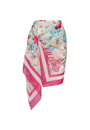 Jupe paréo transparente avec des bordures roses, nouée à la taille, ornée d’un imprimé floral coloré en rouge, bleu et jaune sur fond blanc.
