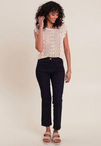 Lichtroze top met kant en een gegolfde mouw, gecombineerd met donkerblauwe broek en nude sandalen met een bandje en een gespsluiting.