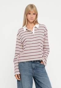Polo à manches longues rayé avec un col blanc, présentant des rayures horizontales maroon et crème. Le tissu semble doux et décontracté.