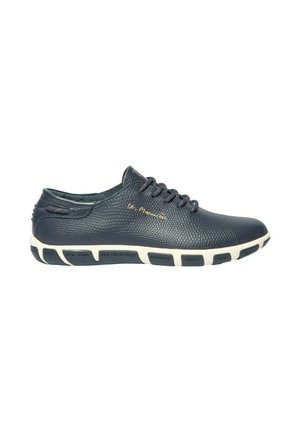 Chaussure décontractée en cuir noir texturé avec laçage à l'avant et semelle blanche affichant des noms de villes imprimés sur des segments noirs.
