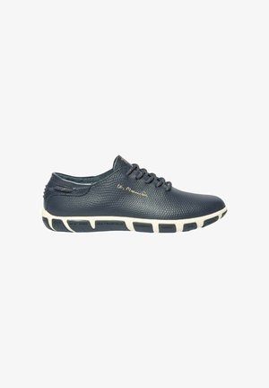 Chaussure décontractée en cuir noir texturé avec laçage à l'avant et semelle blanche affichant des noms de villes imprimés sur des segments noirs.