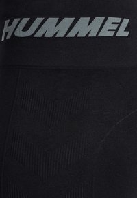Svarta leggings med ett strukturerat chevronmönster och en bred midja med "HUMMEL"-logotypen i silver. Tillverkade av elastiskt tyg.