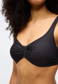 Černý vrchní díl bikin s nazbíraným středovým detailem a zlatými kovovými prvky. Má široká ramínka a hladkou texturu.