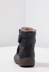 Kinderschoen in navyblauw leer voor de winter, met een bruin fleecvoering, klittenbandsluitingen en een getextureerde rubberen zool, getoond van achteren op een witte ondergrond.