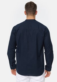 Mornar blue košulja s dugim rukavima, detaljem na leđima i gumbima na manžetama, izrađena od mekanog materijala s glatkom teksturom.
