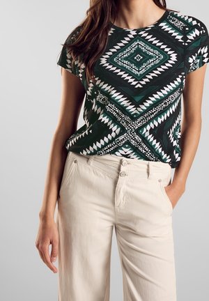 Czarna i zielona koszula z krótkim rękawem w geometryczne wzory, zestawiona z beżowymi, wysokim stanem spodniami z zapięciem na guziki.