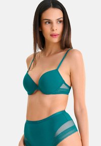 Ensemble en teal comprenant un soutien-gorge et une culotte taille haute. Le soutien-gorge est en tissu lisse avec des bordures en dentelle. La culotte présente des accents en mesh transparent sur les côtés.