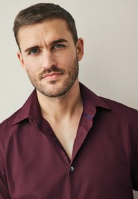 Cămașă button-up bordó cu un model texturat, având un guler ușor deschis și un accent albastru contrastant pe interiorul gulerului.