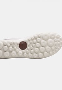 Vit gummisula med rundade greppmönster och en brun cirkulär logotyp. Texturerad yta förbättrar greppet. Rundade kanter för komfort.