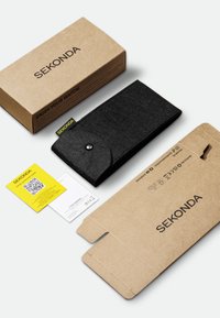 Étui en feutre noir avec fermeture à bouton-pression, étiquette jaune. Boîte en carton brun avec "SEKONDA" imprimé, comprend une carte de garantie et un code QR.