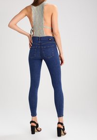 Blå denim skinnyjeans med hög midja, tillsammans med en topp med spetsbakdel som har scallopkant och justerbara axelband. Svarta klacksandaler.