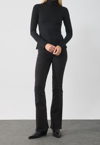 Svart långärmad turtlenecktröja i kombination med svarta utsvängda jeans och spetsiga svarta ankelstövlar, med en slät textur och en åtsittande design.