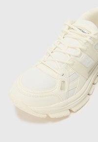 White athletic shoe with a textured mesh upper and smooth synthetic accents. Features a cushioned sole and traditional lace-up design.