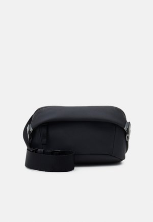 Sac rectangulaire noir en matériau lisse, doté d'une large bandoulière ajustable et d'une fermeture latérale à boucle. Design minimaliste sans motifs.
