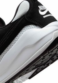 Baskets Nike noir et blanc avec tige en mesh, semelle intermédiaire blanche épaisse et semelle extérieure noire texturée affichant le logo Nike sur le talon.