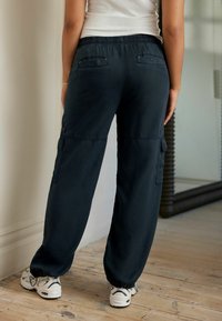 Pantaloni cargo blu navy con vita elastica, tasche laterali e orli a polsino, realizzati in tessuto morbido, abbinati a sneakers bianche.