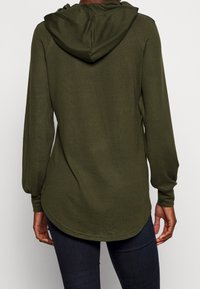 Mörkgrön huvtröja med långa ärmar, en rundad nederkant och en mjuk yta. Har en avslappnad passform och detaljer vid sidsömmarna.