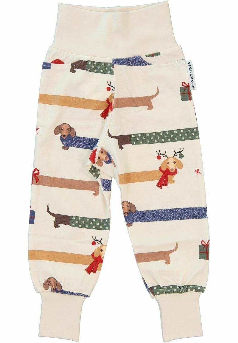 Teddybyxor för små barn i bomull med elastisk midja, i en ljus kremfärg med färgglada illustrationer av taxar och festliga detaljer.