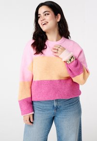 Pull tricoté à rayures roses, jaunes et violettes. Présente un col arrondi et des manches longues légèrement évasées.