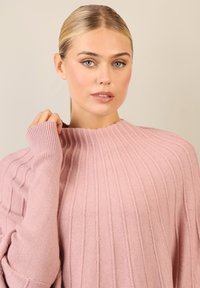 Helle rosa, gerippter Strickpullover mit hochgeschlossenem Kragen und langen Ärmeln, die einen gewellten Saum haben. Weicher Textur,lässige Passform.