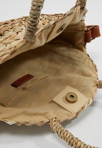 Borsa in paglia intrecciata con interno beige testurizzato, dotata di etichetta in pelle, fodera in tessuto e chiusura a scatto magnetico. Due manici intrecciati.