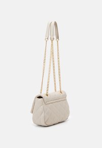Bolso de mano acolchado en color beige con forma estructurada, asas de cadena doradas y cierre de solapa. Textura suave con un patrón de diamantes en toda su superficie.