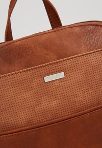 Sac à main en cuir marron avec surface texturée, comprenant un panneau lisse et une plaque logo en métal. Fermeture éclair sur le dessus.