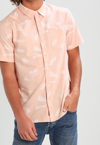Hellrosa Kurzarm-Hemd mit Knopfleiste, weißen grafischen Mustern, darunter Logos und Palmen. Mit Brusttasche und Kragen.
