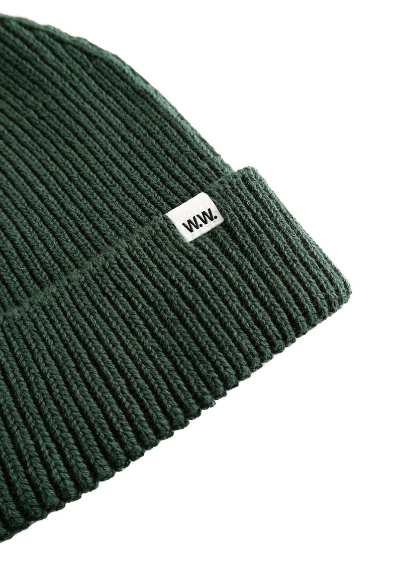 Groene geribbelde gebreide beanie met een opgevouwen rand, voorzien van een klein wit label met de tekst "W.W." aan de voorkant.