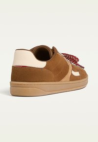 Sneaker in suede marrone con tallone in pelle crema, lacci a fantasia rossa e suola in gomma. Presenta dettagli cuciti e un design low-top.