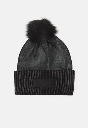 Bonnet noir tricoté avec un revers côtelé, un gros pompon duveteux sur le dessus et une étiquette de marque rectangulaire sur le revers.