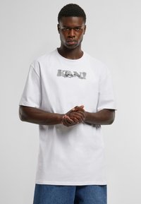 White cotton t-shirt with a round neckline and short sleeves, featuring a stylized gray graphic text "KAN" at the center.
