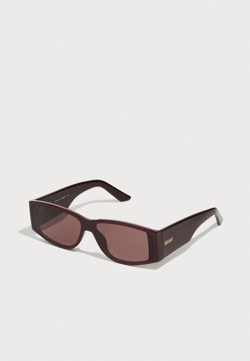 Burgundy rectangular sunglasses with dark lens, plastic frame, and gold "QUAY" logo on the arm. Smooth texture and minimalist design.