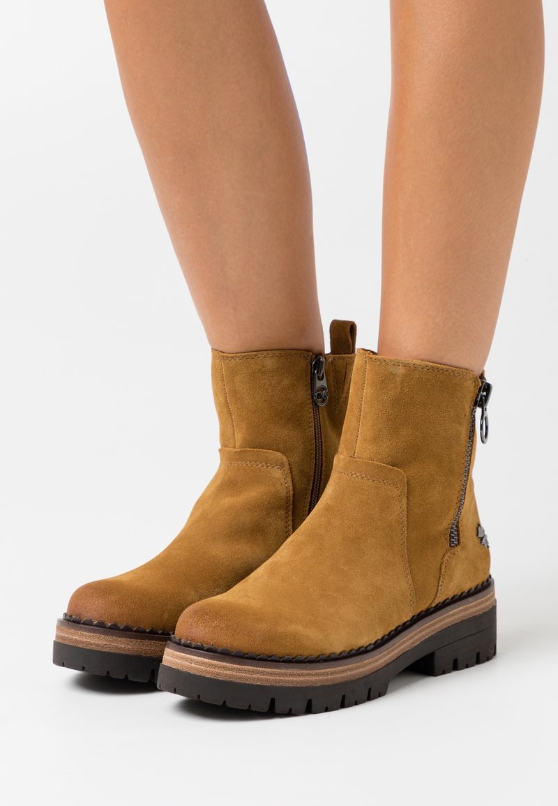 Tan suede ankle boots with a side zipper, round toe, and black rubber sole; features a contrasting tan midsole and stitching details.