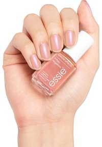 Vernis à ongles rose doré dans un flacon en verre transparent avec un bouchon blanc, tenu dans une main avec des ongles soigneusement manucurés, montrant une finition douce et scintillante.