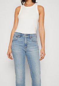 Vit ribbad tanktopp med hög krage, kombinerad med ljusblå raka jeans som har framfickor och en knappstängning.