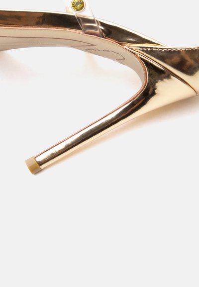 Χρυσό μεταλλικό γοβάκι με λεπτό τακούνι στιλέτο και λουράκι στον αστράγαλο με μικρή στρογγυλή αγκράφα.