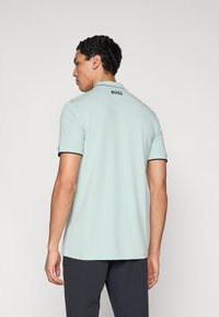 Svetlozelené polokošeľa s čiernymi akcentmi na golieri a rukávoch. Na zadnej strane je uvedené logo "BOSS", elegantný dizajn a krátke rukávy.