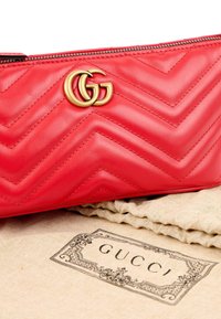Pochette en cuir matelassé rouge avec logo double G doré reposant sur un sac anti-poussière beige de marque Gucci avec bordure décorative.