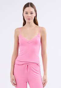 Débardeur rose à côtes avec une bordure en dentelle au niveau du décolleté. Présente des bretelles fines et une coupe ajustée, complété par un pantalon rose assorti.